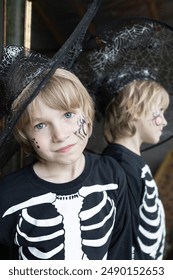 boy in a skeleton costume and a black hat stands near a mirror. Halloween celebration. Trick or treat. Mysterious, festive image of a witch for the holiday