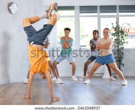 Boy skillfully performs handstand standing on hands upside down during break dance workout. Multiracial group of boys and girls perform basic movements in studio