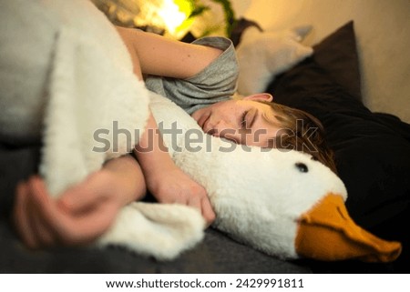 a boy is sleeping in the bed with his large soft toy goose