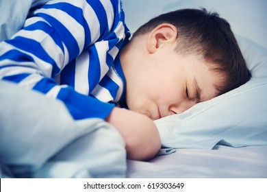 Boy Sleeping In Bed In Pajamas. Child Lying In Bed On Pillow At Night