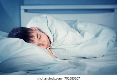 Boy sleeping in bed in pajamas. Child lying in bed on pillow at night