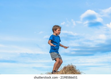 Boy Smile Play Dance Grimace Show Off Blue T-shirt Stand On Haystack Bales Of Dry Grass, Clear Sky Sunny Day. Balance Training. Concept Happy Childhood, Children Outdoors, Clean Air Close To Nature