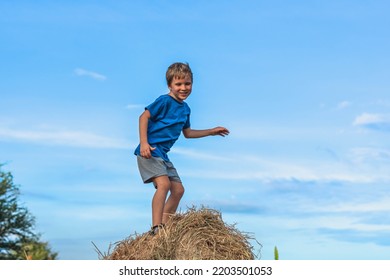 Boy Smile Play Dance Grimace Show Off Blue T-shirt Stand On Haystack Bales Of Dry Grass, Clear Sky Sunny Day. Balance Training. Concept Happy Childhood, Children Outdoors, Clean Air Close To Nature