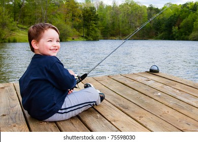 Boy Smiles While Fishing From Dock On Lake.