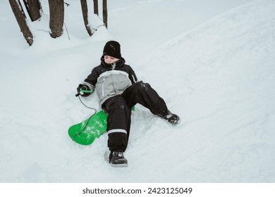 A boy snowboards in a winter snowy forest and falls - Powered by Shutterstock