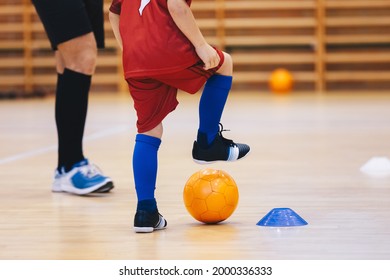 Boy in Soccer Clothes with Ornage Futsal Ball. Kid on indoor soccer training with coach. Child playing futsal on wooden floor. Futsal school practice with coach trainer