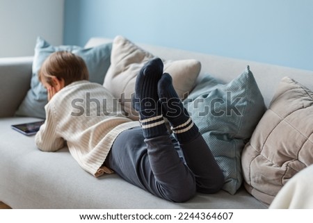 Boy spends time behind a screen on a tablet on the sofa in the living room. Digital device. Technologies.