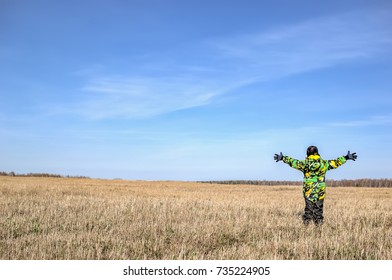 Boy spread arms to the side standing on a rustic autumn yellow field. Blue sunny sky. Rear view.