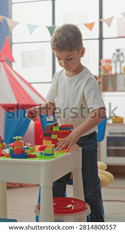 Boy stacking colorful plastic blocks on a low table with his right hand in a bright playroom tent area; quiet concentration.
