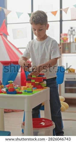 Boy stacking colorful plastic blocks on a low table with his right hand in a bright playroom tent area; quiet concentration.