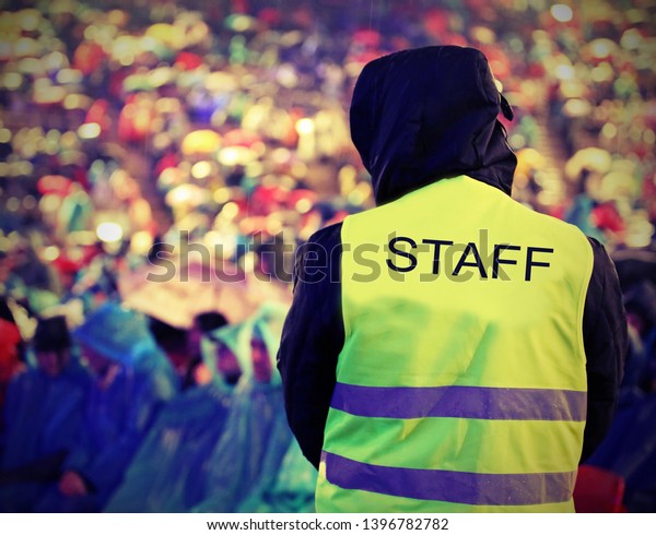 boy of Staff\
with high visibility jacket during live outdoor concert when it is\
raining with old toned\
effect