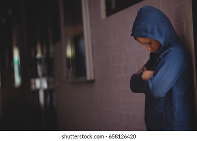 Boy Standing Alone By Wall In Corridor At School