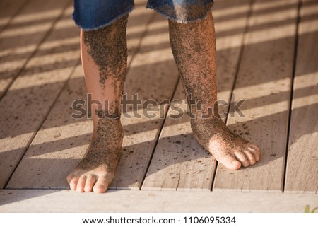 Boy is standing in jeans on wooden floor his legs covered with sea sand.