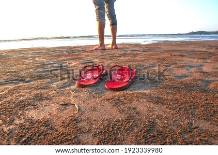A boy standing on beach beside flip flops, a jogger standing on beach near a flip flop and water  preparing to start running 