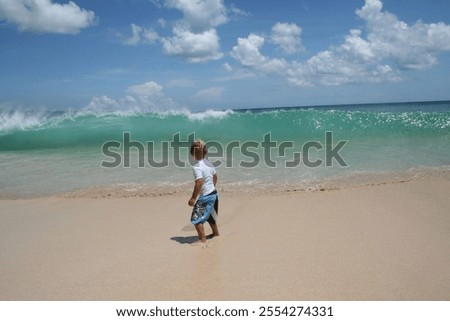 Boy standing on a beach looking at a large wave