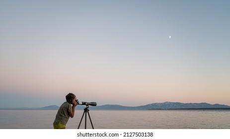 Boy Standing On The Beach In The Summer Evening Looking Through The Telescope Exploring.