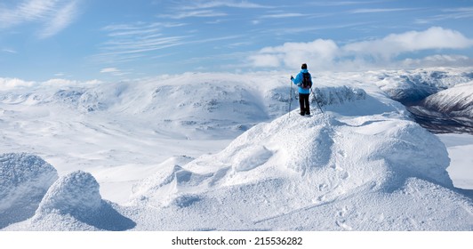 A boy standing on a snow and ice covered summit having a magnificent view towards a valley in the Norwegian mountains at easter at a sunny day With few clouds in background