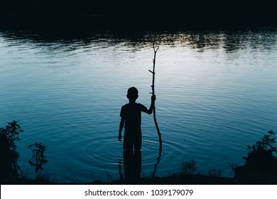 Boy Standing In The River At Night. Kid With A Stick Comes Into The Water In The Dark. Copy Space For Your Text