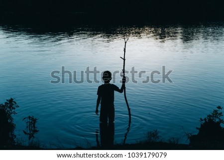 boy standing in the river at night. kid with a stick comes into the water in the dark. Copy space for your text