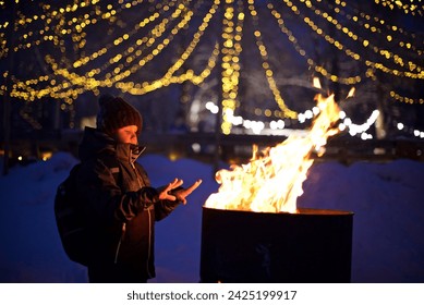 A boy stands by the fire to keep warm in the winter cold night park