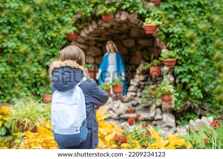 a boy stands in front of a statue of the Holy Virgin Mary and prays