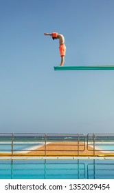 Boy Stands On A Diving Platform About To Dive Into The Swimming Pool. Boy Standing On High Diving Spring Board Preparing To Dive.