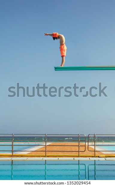 Boy stands on a diving platform about to dive into\
the swimming pool. Boy standing on high diving spring board\
preparing to dive.