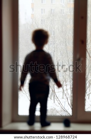 Boy stands on the windowsill and looking through the window.