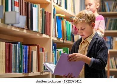 boy stands reading a book against multi colored bookshelf in library, getting knowledge