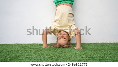 A boy stands upside down against a white wall