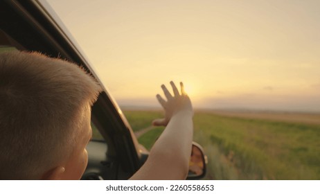 Boy stretches out his hand from car window catch sun glare of sunset, happy emotions. Children's dreams, play. Happy teenager guy rides in car, waving his hand out car window. Road travel concept - Powered by Shutterstock