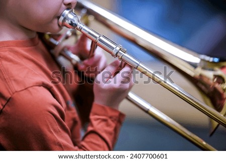Boy student playing and practicing trombone for school band performance. Music education instrument background. 