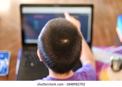 Boy Studying Online Course At Home By Using Laptop And Pointing To Touch Screen To Interact With Class. Home Online Learning During Covid-19 Breakout Concept.