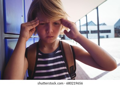 Boy suffering from headache while standing by lockers in corridor at school - Powered by Shutterstock