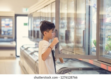 Boy In The Supermarket Standing In Front Of The Freezer Near The Glass Doors 