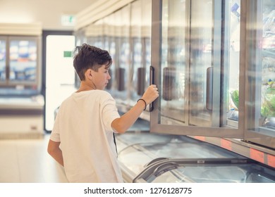 Boy In The Supermarket Standing In Front Of The Freezer Near The Glass Doors  