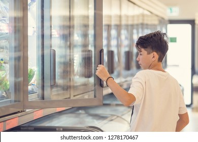 Boy In The Supermarket Standing In Front Of The Freezer Near The Glass Doors 