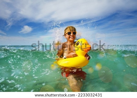 Boy swimming in ocean waves in orange sunglasses with yellow inflatable duck playing in water