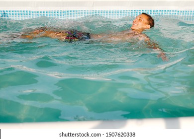 Boy Is Swimming On The Water, Floating, In The Swimming Pool