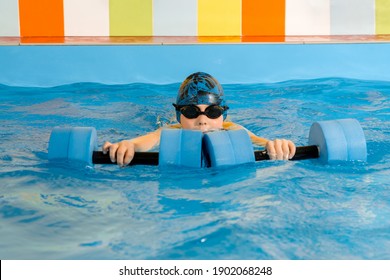 Boy swimming with water dumbbells in hands in swimming pool