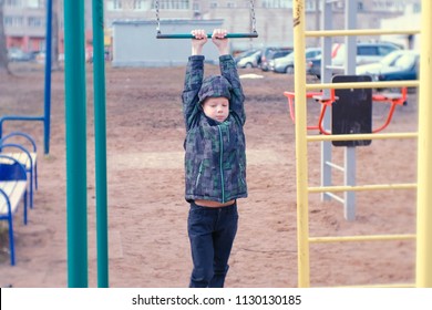 Boy Swings On A Gymnastic Trapeze, Jumps And Fall On Sand. Playground In The Courtyard Of The City House.