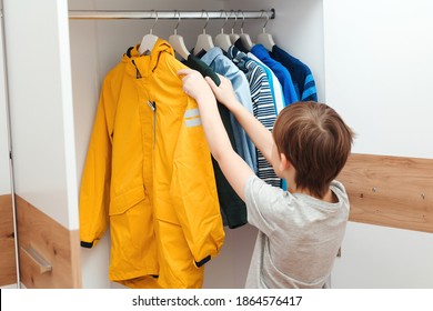 Boy Taking Jacket From Hanger Stand. Wardrobe With Child's Clothing. Cute Boy Get Dressed In The Morning For School. Kid Organizing Clothes In Wardrobe.