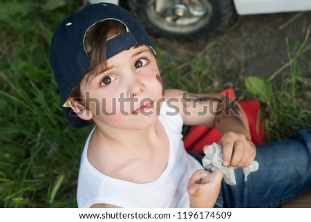 A boy in a tank, jeans and a baseball cap in the garage repairing the car.