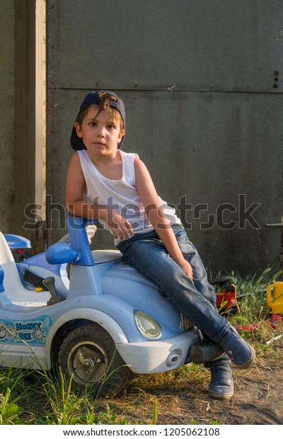 A boy in a tank, jeans and a baseball cap in the\
garage repairing the car.