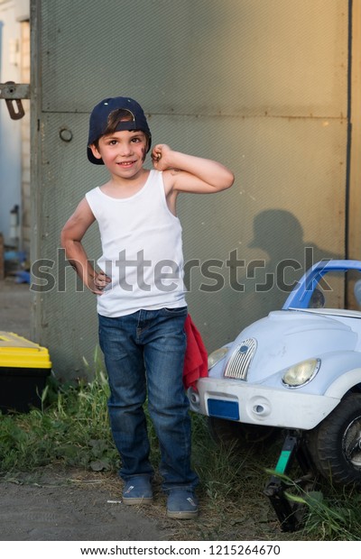 A boy in a tank, jeans and a baseball cap in the
garage repairing the car.