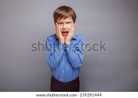 boy teenager European appearance holds hands the person opened his mouth on a gray background