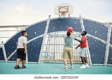 Boy throwing ball into basketball hoop under fathers control while playing basketball with brother on sports ground