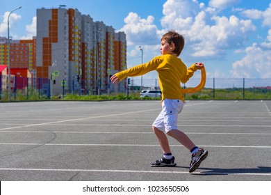 The Boy Throws A Boomerang Into The Blue Sky. The Kid Plays With A Boomerang On The Playground. Children's Outdoor Sports Games