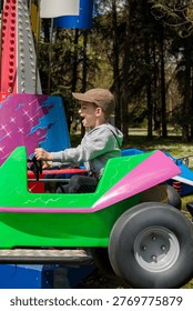 a boy throws his head back screaming with pure excitement while gripping the wheel of a bright green and pink carnival car ride beside a colorful illuminated tower