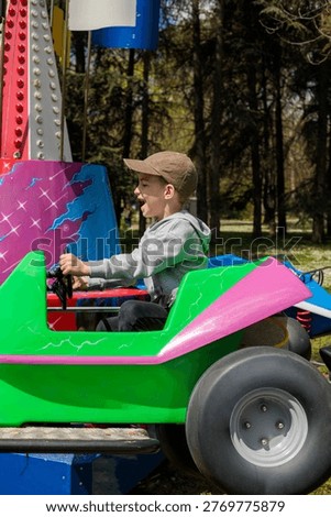 a boy throws his head back screaming with pure excitement while gripping the wheel of a bright green and pink carnival car ride beside a colorful illuminated tower